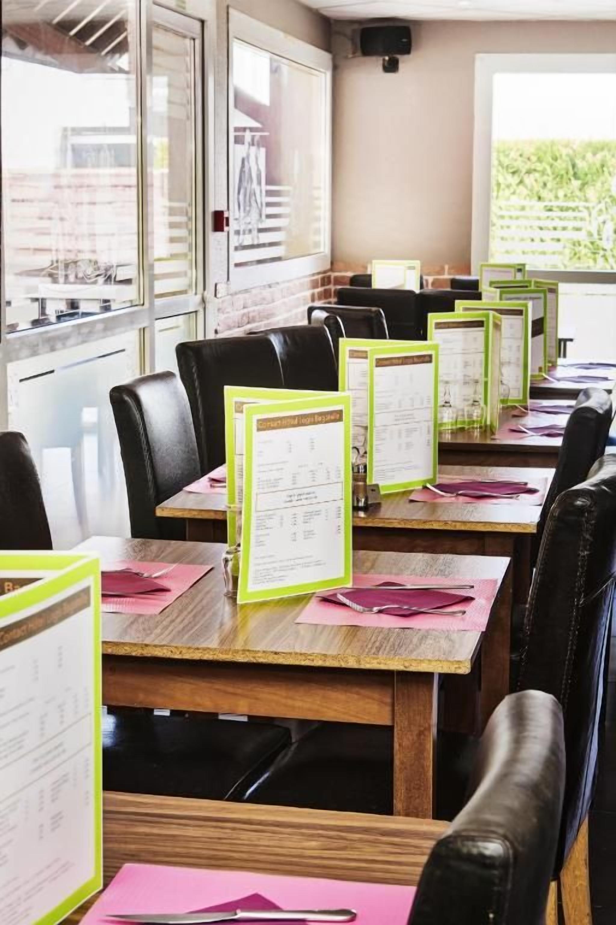 Un comedor con mesas de madera, sillas de cuero negro y menús en atril.
