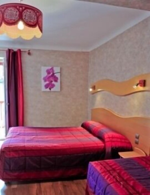 Habitación de hotel con dos camas, cabecera de madera, una obra de arte colgada en la pared y una ventana con cortinas rojas.