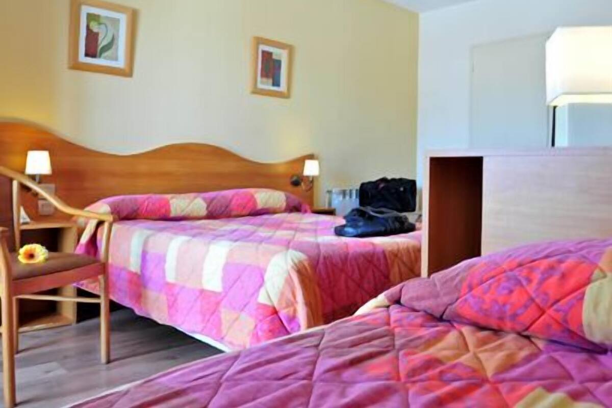 A hotel room with two beds, wooden headboards, and a nightstand with a lamp.