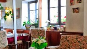 Una habitación con techo de madera, una mesa redonda con un florero, sillas de estampado floral y un área de comedor visible a través de un separador de vidrio.