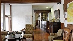 Un vestíbulo de hotel con techo de madera, un área de comedor con una mesa redonda, sillas estampadas y una cocina con barra.
