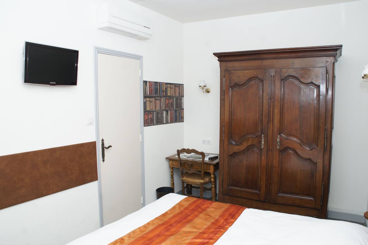 A bedroom with a bed, a wardrobe, a desk with a chair, a television, and a bookshelf.