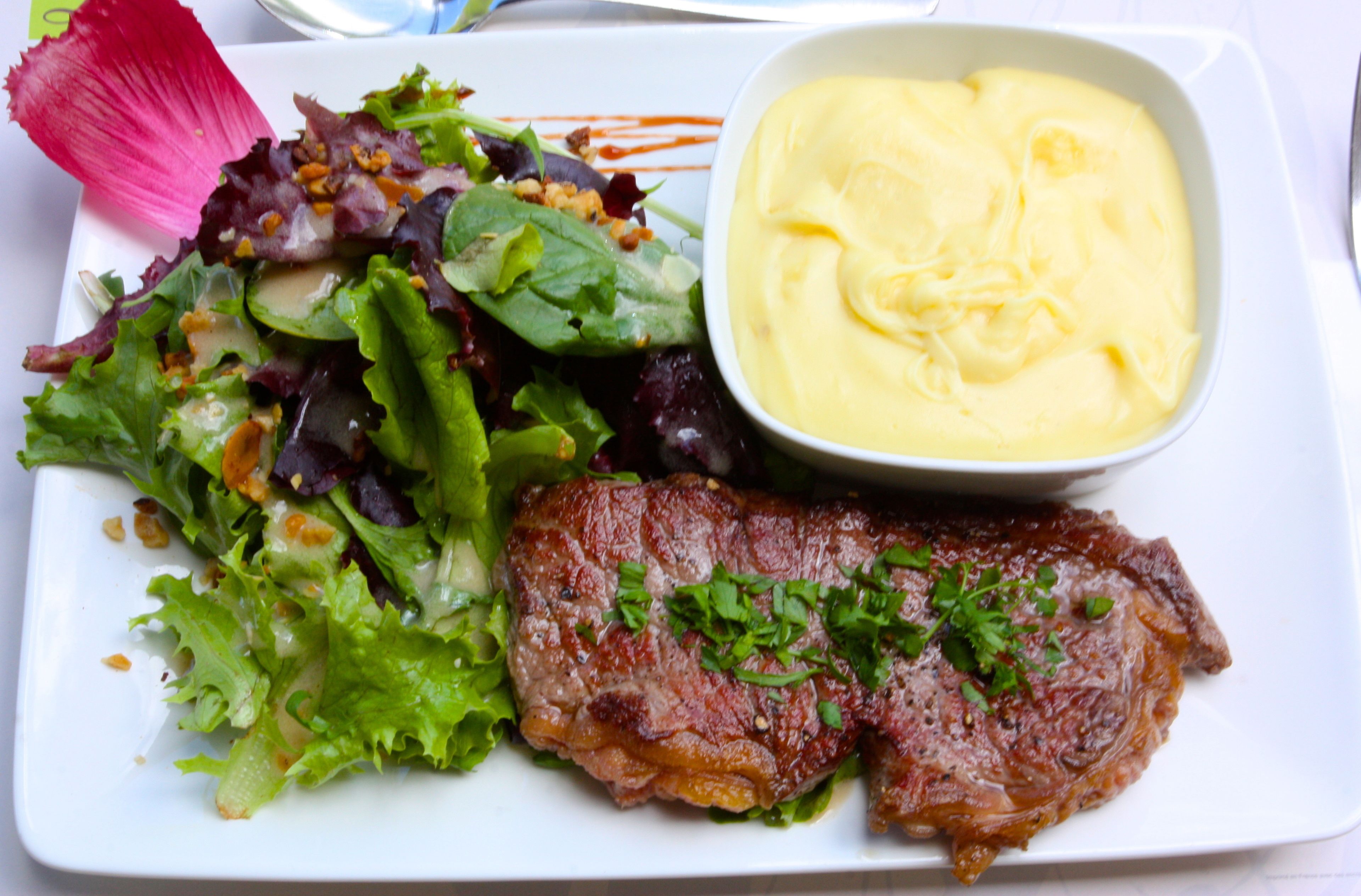 Une assiette avec un steak, une salade et une sauce crémeuse.