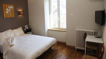 Ein Schlafzimmer mit Bett, kleinem Tisch, Stuhl, Heizkörper, Fernseher und Fenster mit Blick auf Bäume.