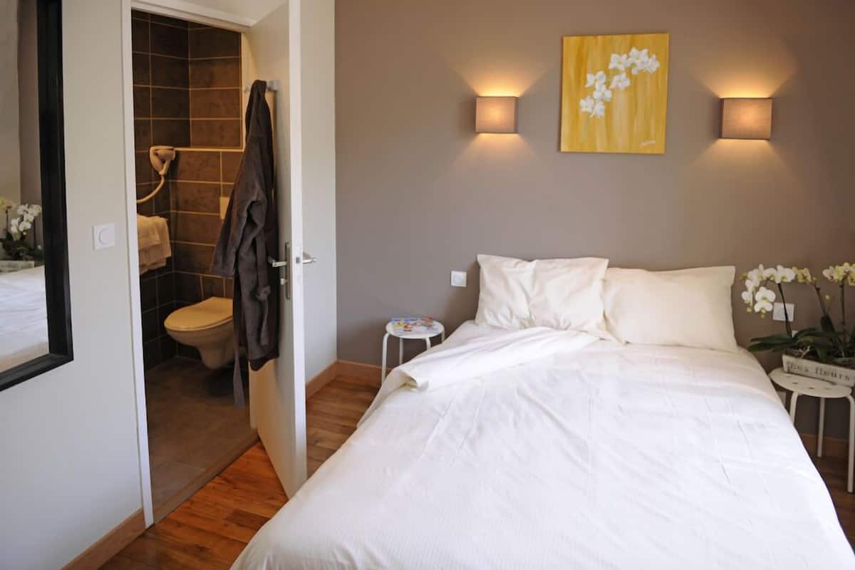 Ein Schlafzimmer mit Bett, Nachttisch, kleinem Tisch, Wandleuchte und einem Gemälde.