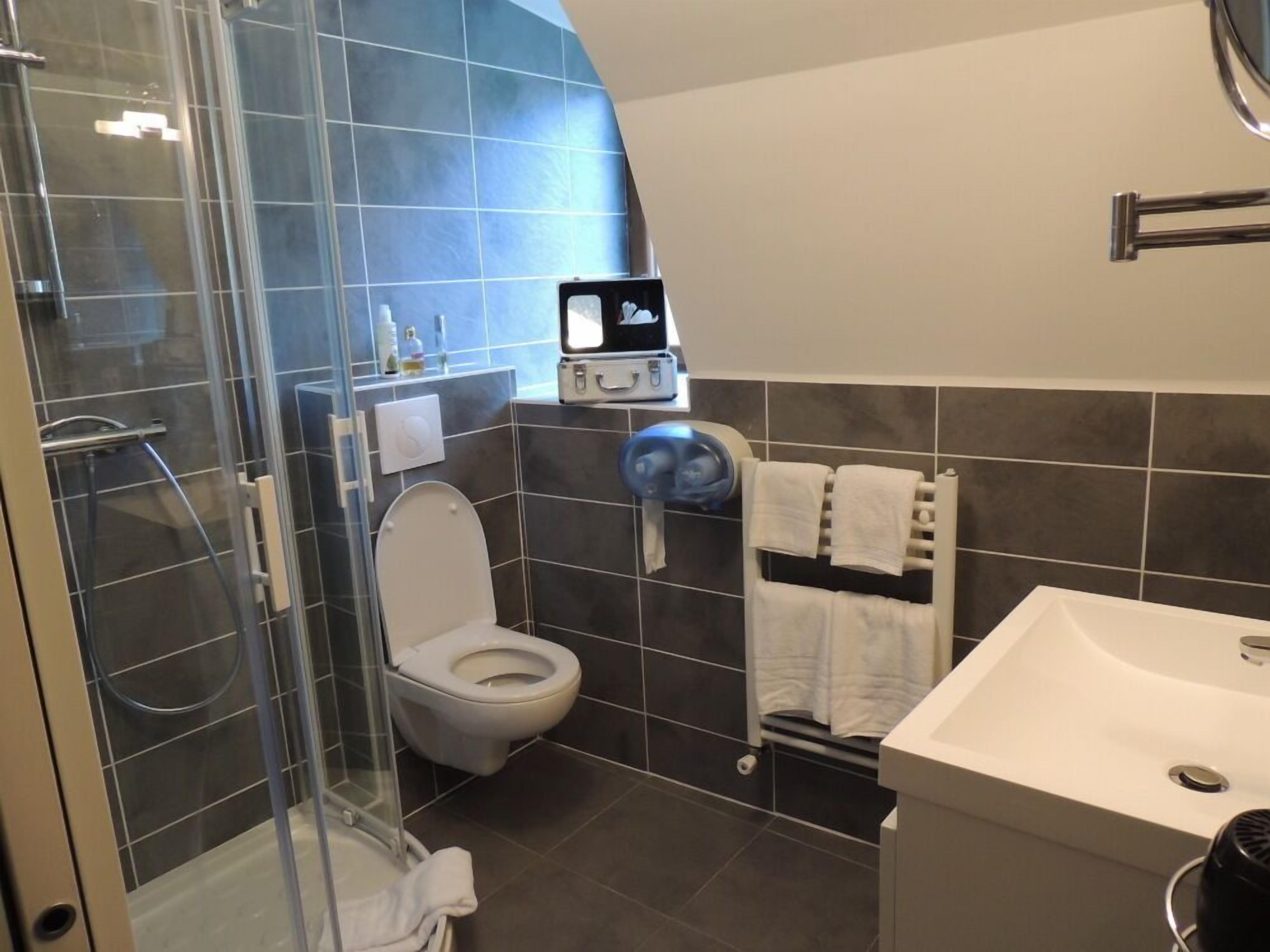 Un baño moderno con ducha envuelta en vidrio, inodoro blanco, lavamanos y toallero.