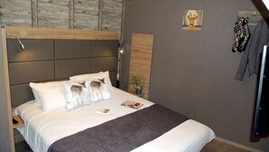 Una cama bien hecha con cabecera, una lámpara de pared, un cuadro y un perchero.