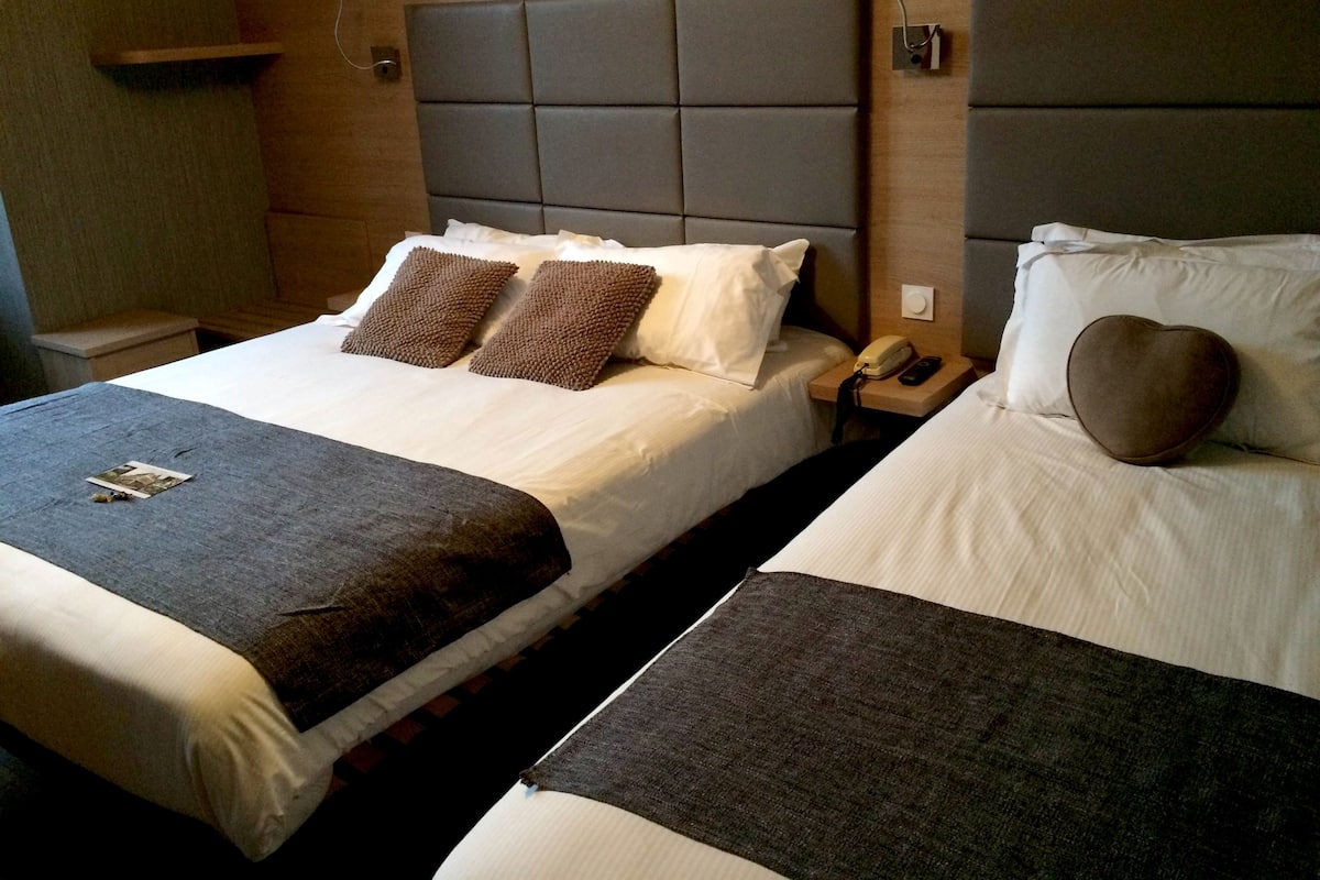 Ein Hotelzimmer mit zwei Betten, jeweils mit einem Kopfteil, einem Nachttisch mit Telefon und einer Decke.