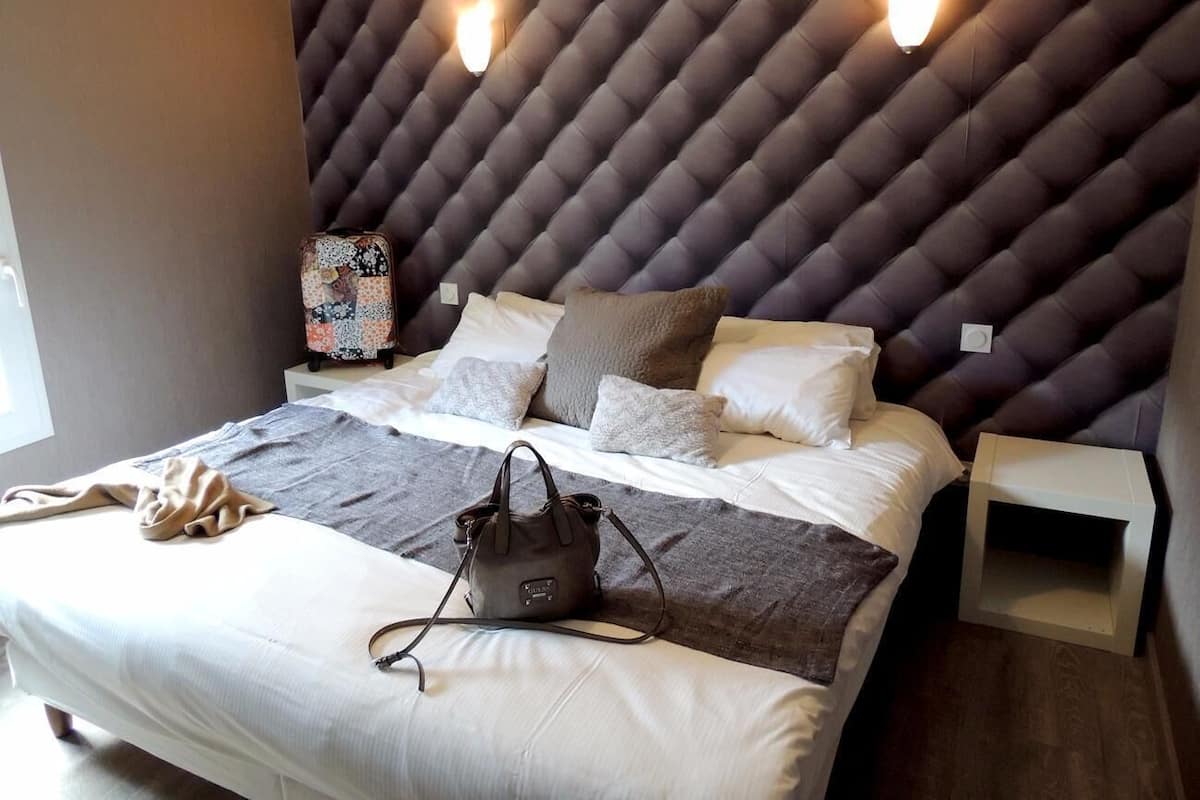 Ein modernes Schlafzimmer mit einer gepolsterten Kopfteile, einem Bett mit weißen Leinen, einer grauen Tagesdecke, einer braunen Handtasche und zwei Nachttischen.