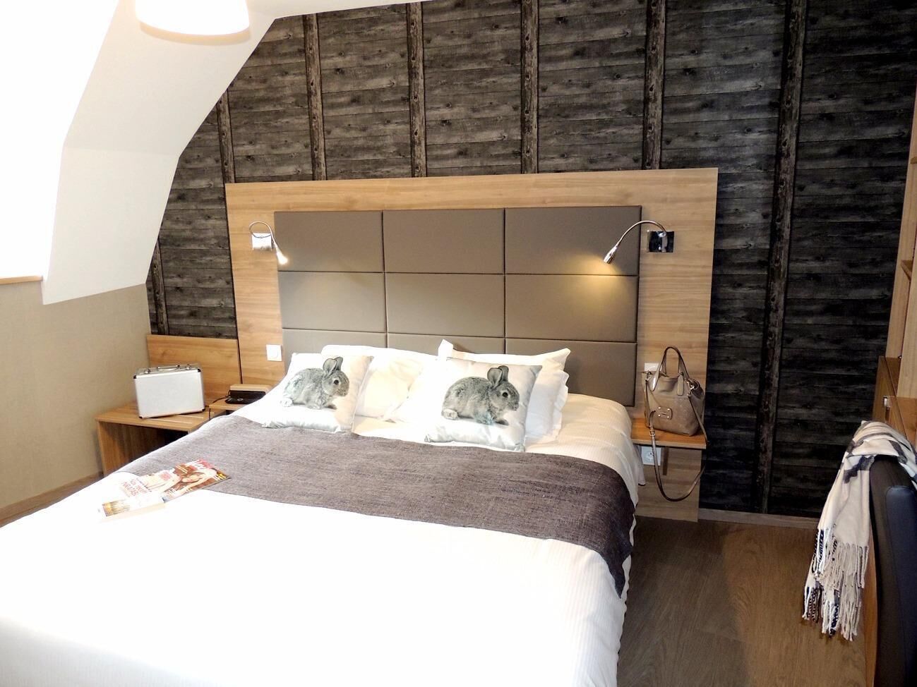 Una habitación de hotel con una cama, una mesita de noche, una lámpara y un cabecero de madera.