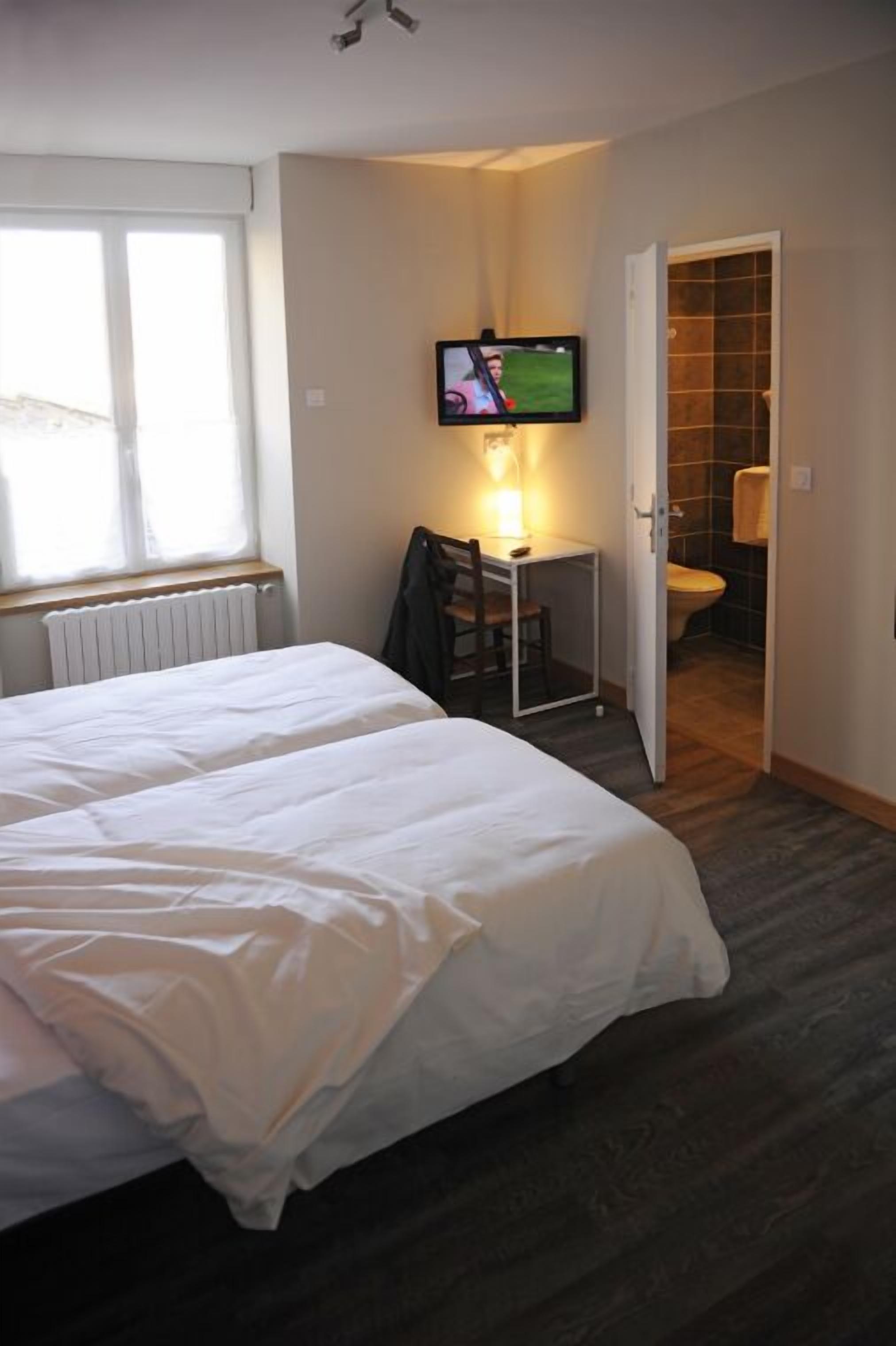 A hotel room with two beds, a desk with a chair, a television, and a bathroom visible through an open door.