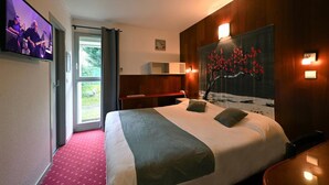 Habitación de hotel con una cama grande, un televisor montado en la pared, un cuadro y una ventana con cortinas.
