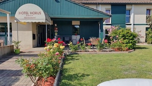 Hotel Horus, con un letrero sobre la entrada, un área de estar exterior cubierta y un jardín con diversas plantas y flores.