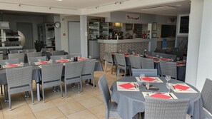 Ein Restaurant mit mehreren Tischen und Stühlen, einer Bar und einer Küche im Hintergrund.