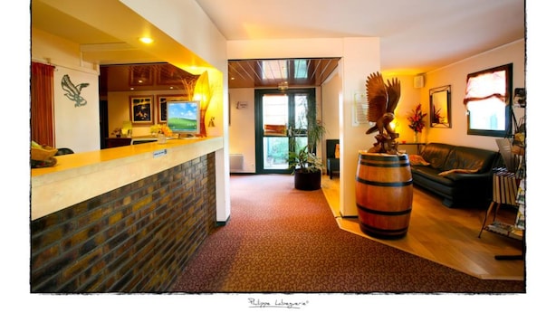 Un vestíbulo de hotel con mostrador de recepción, un sofá de cuero, un barril de madera grande y una planta en maceta.