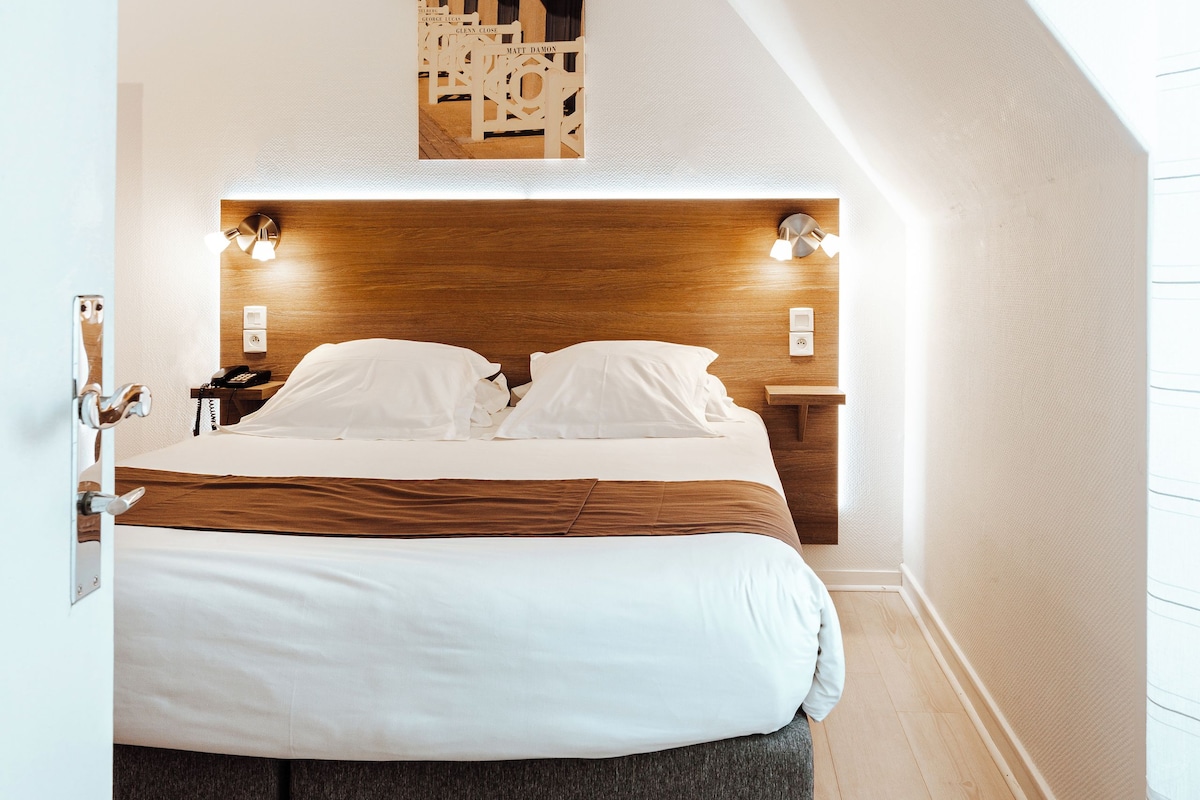 A bedroom with a wooden headboard, a bed with white bedding, two bedside tables, and a wall-mounted light fixture.