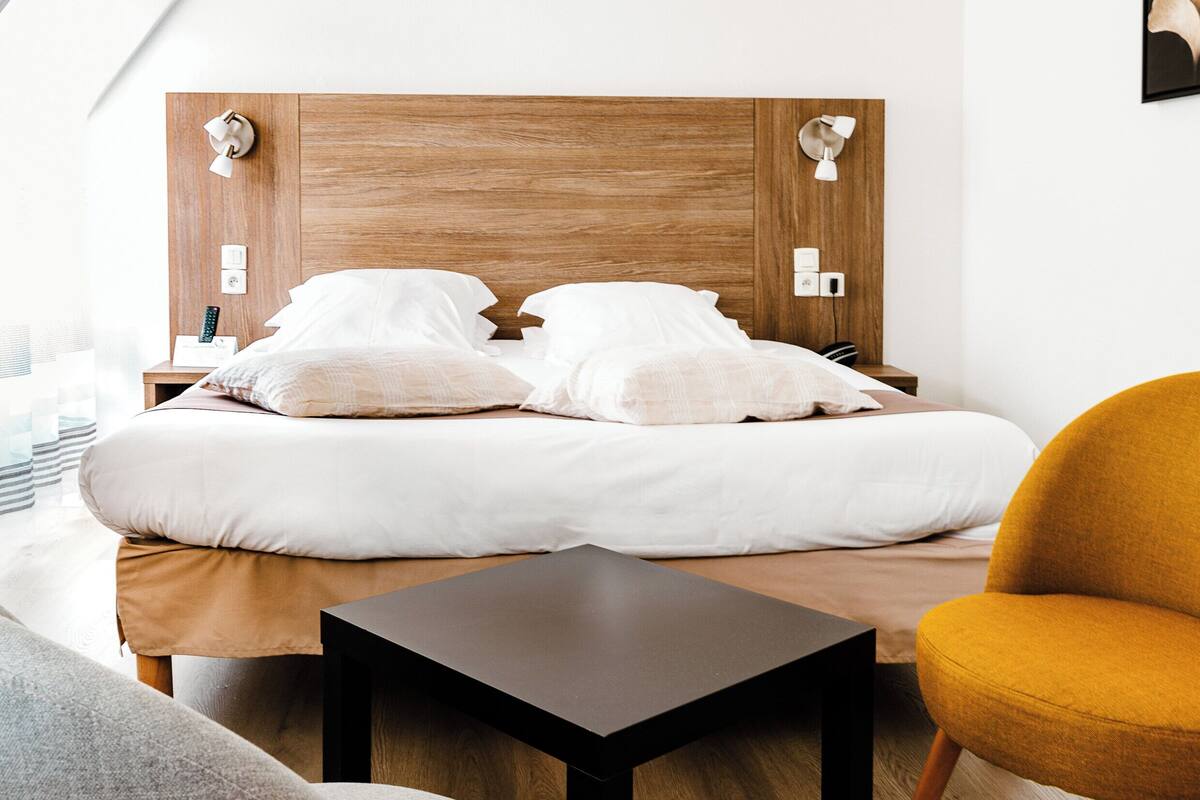 A modern bedroom with a wooden headboard, a bedside table, a chair, and a small table.