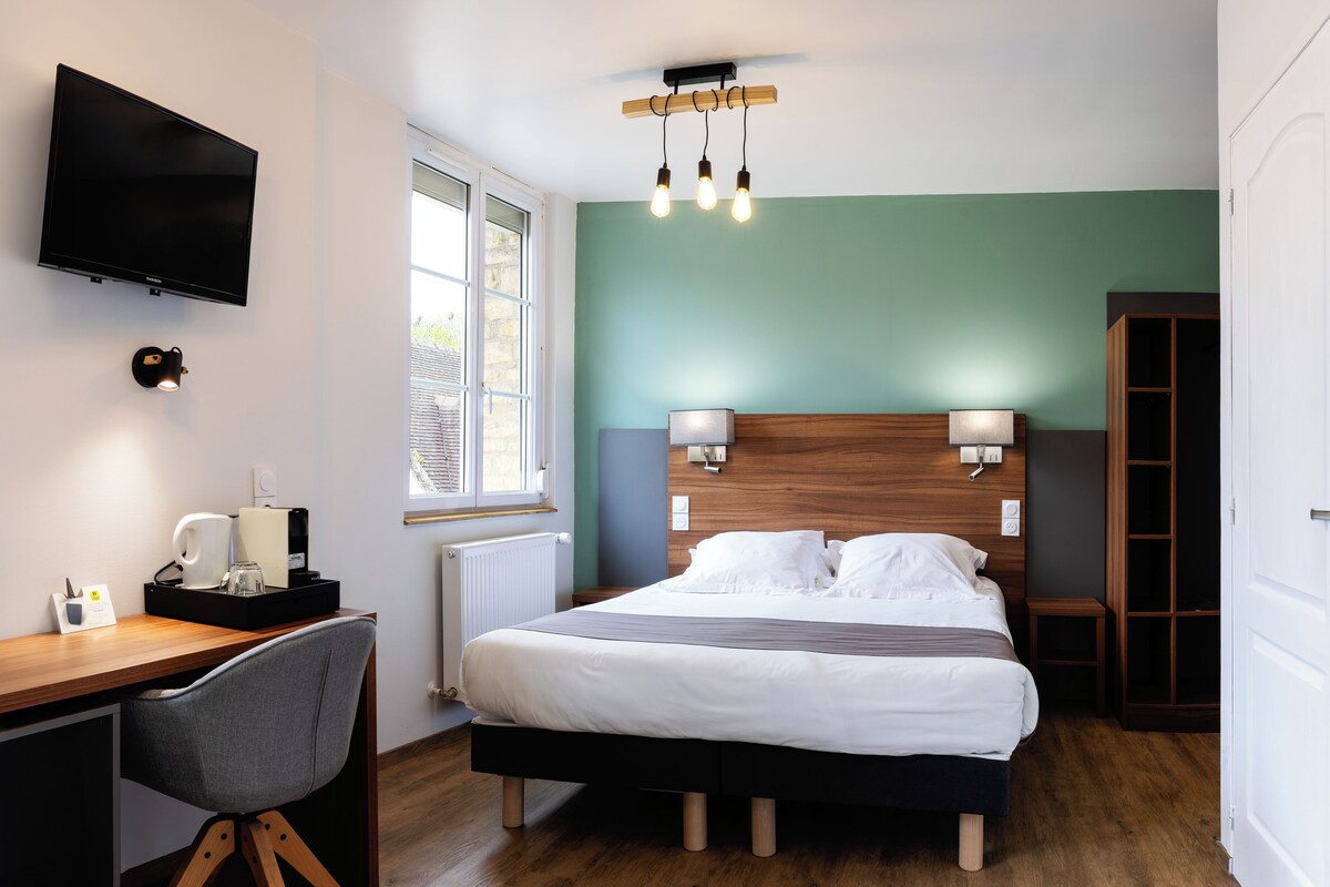A hotel room with a bed, desk, chair, TV, bedside lamps, and a window.