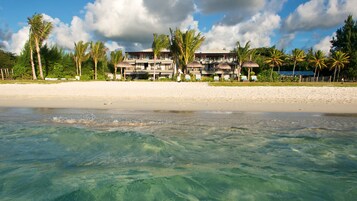Un hotel frente a la playa con varios balcones, palmeras y aguas turquesas cristalinas.