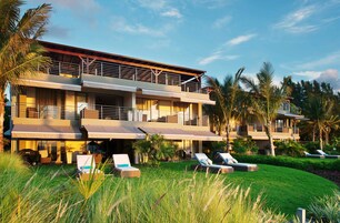 Un resort de varios pisos con un área exterior cubierta, palmeras y sillones de descanso.