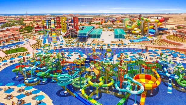 A water park with multiple slides and pools, surrounded by buildings and a clear sky.