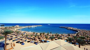 A beach resort with numerous sun loungers, umbrellas, and palm trees.