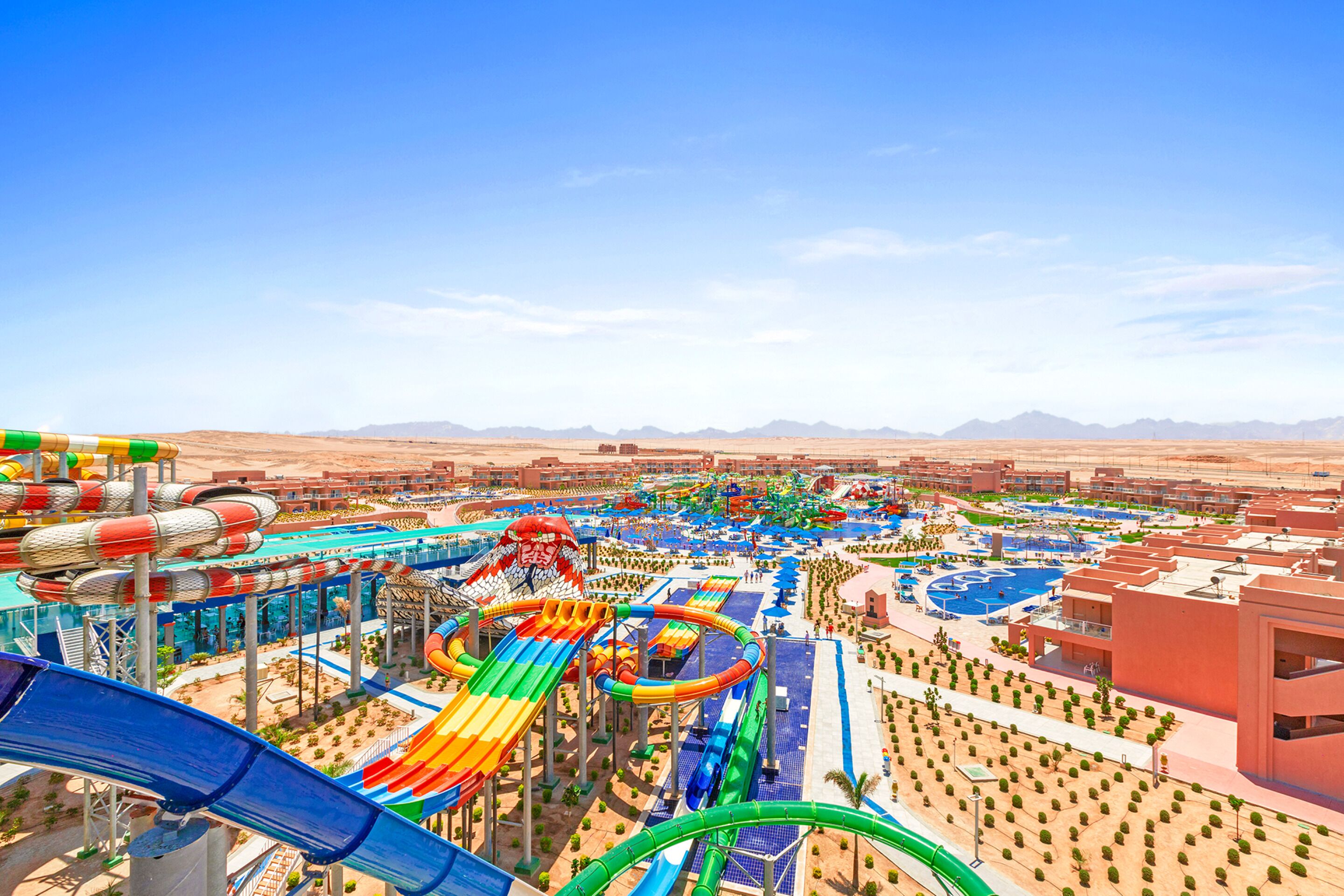 Een waterpark met glijbanen en zwembaden, omringd door een woestijnlandschap en bergen.