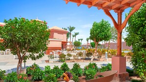 An outdoor seating area with wicker chairs and a table, surrounded by greenery and a clear view of the street.