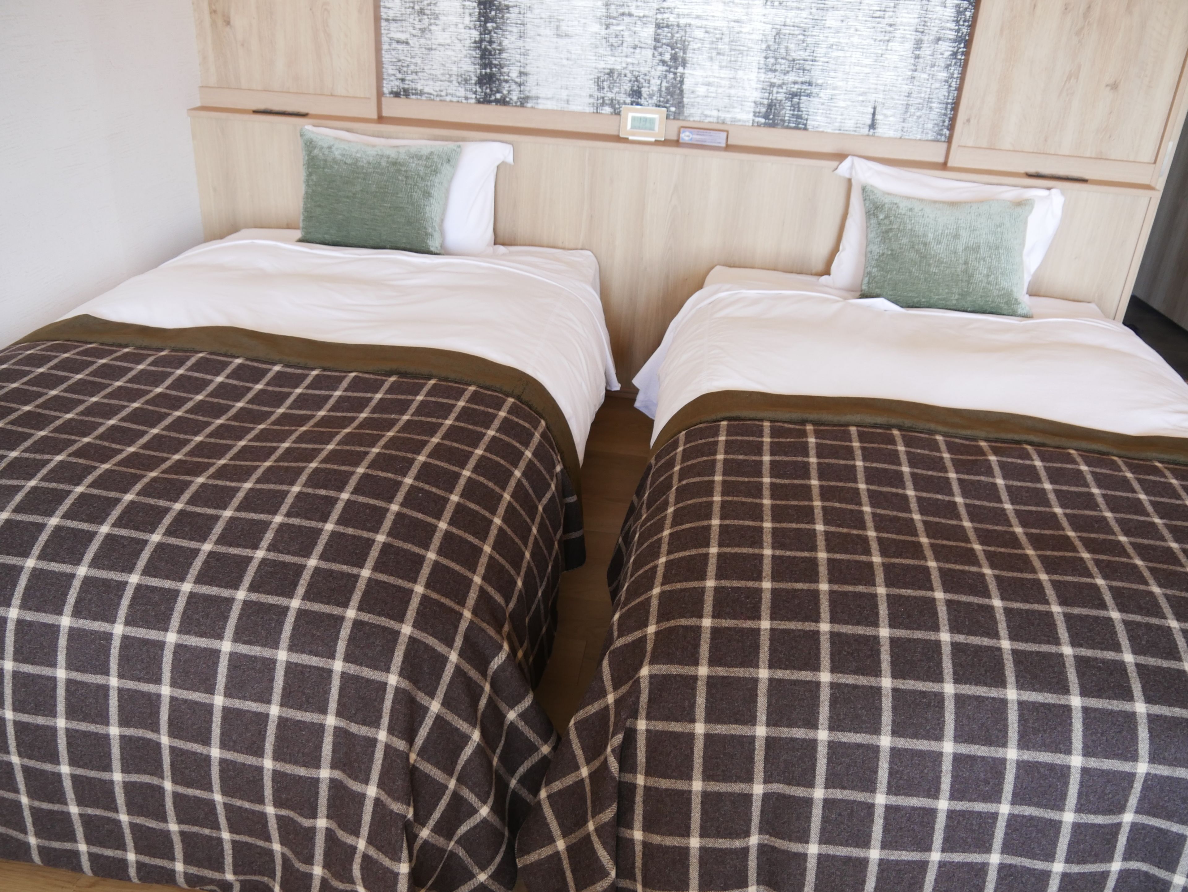 A double room with two beds, each with a checkered bedspread and pillows, a wooden headboard, and a small clock.