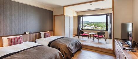 Ein Hotelzimmer mit zwei Betten, einem Schreibtisch, einem Fernseher und Blick auf eine Stadtlandschaft.