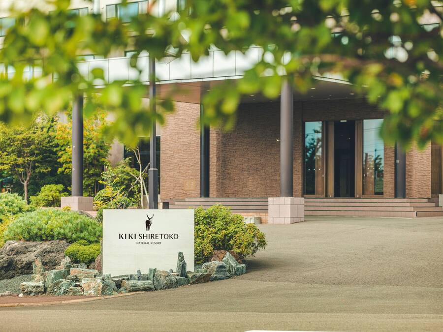 A building entrance with a sign reading 'KIKI SHIRETOKO NATURAL RESORT' and a landscaped area with rocks and shrubs.
