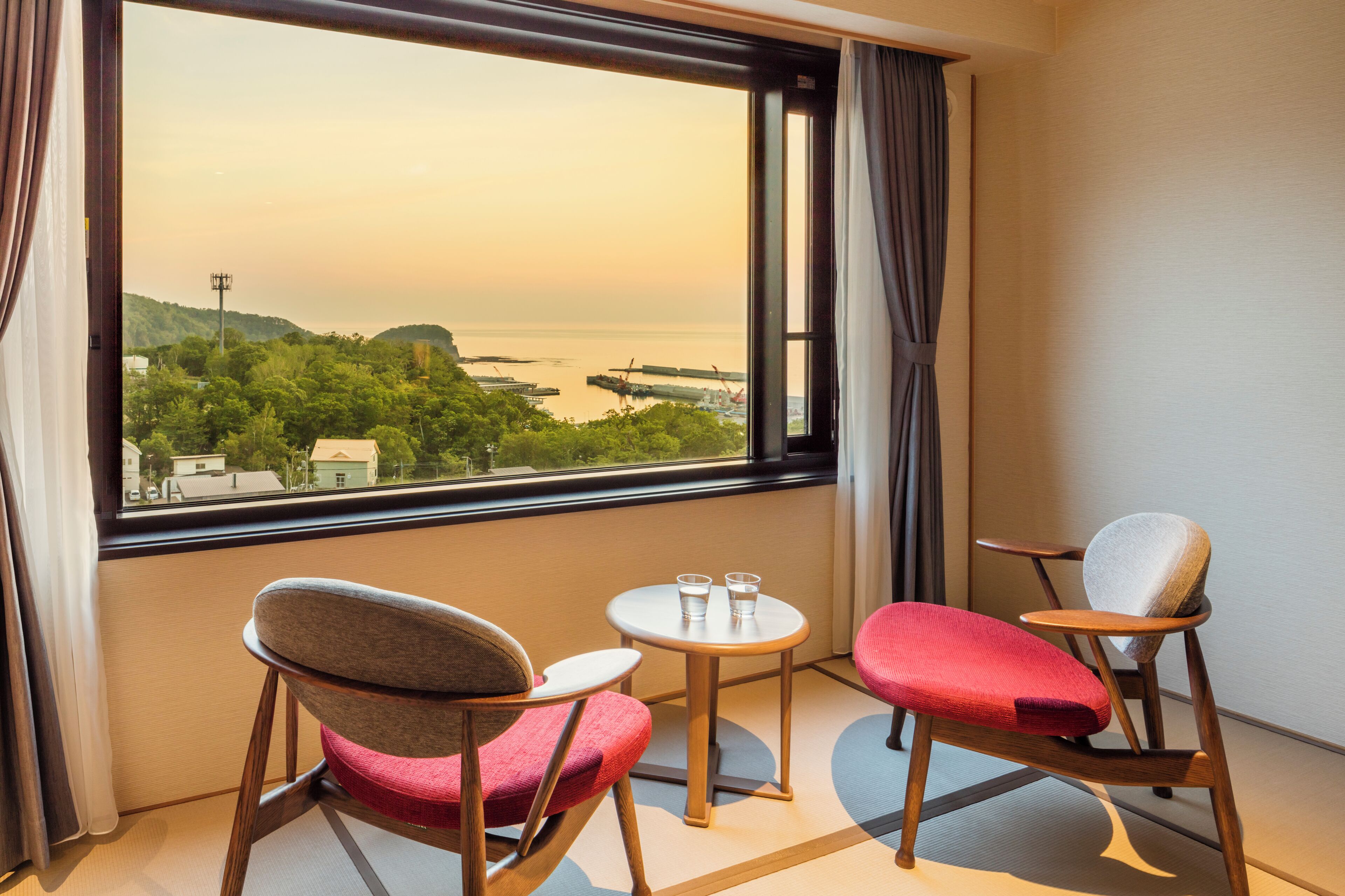 A room with a large window, two chairs, a small table, and a view of a coastal landscape.