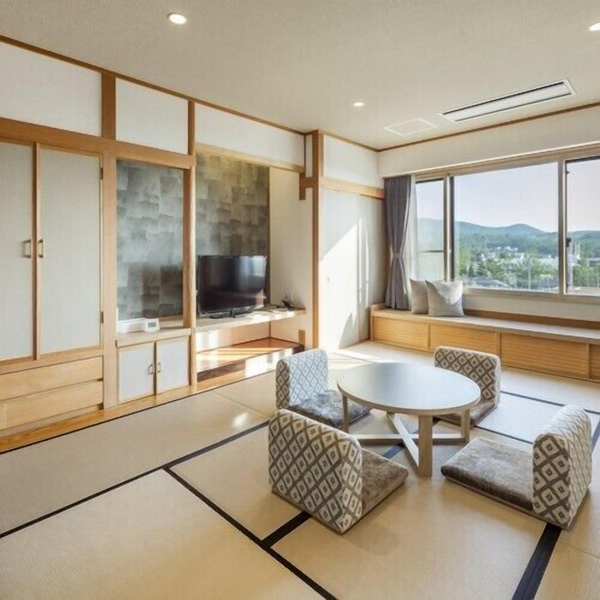 Ein traditioneller japanischer Raum mit Tatami-Boden, einem niedrigen Tisch mit Kissen und einem Fernseher an einer niedrigen Wand.