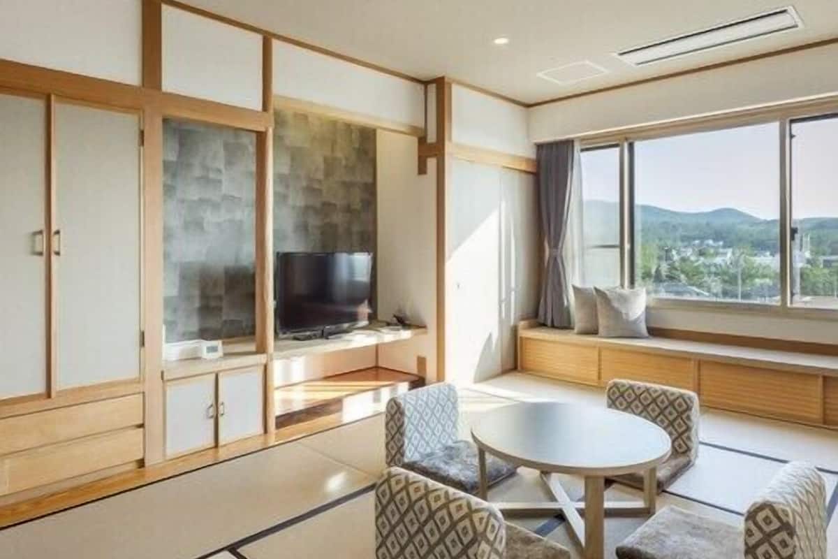 A traditional Japanese-style room with tatami flooring, a low table with cushions, and a television on a low wall.