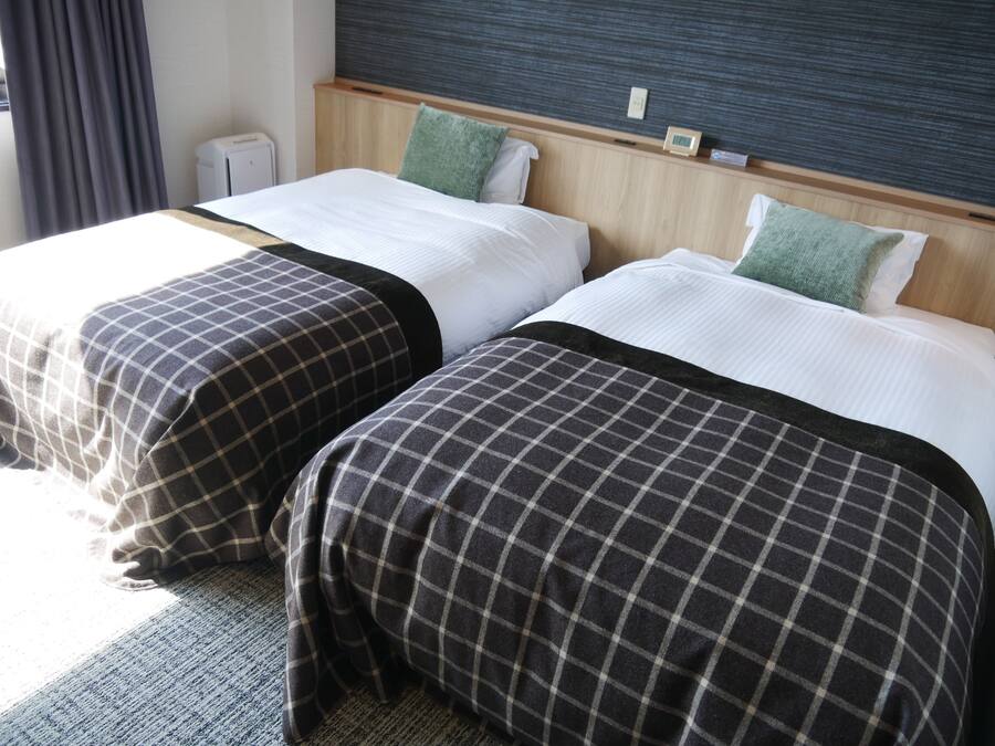 Two single beds with checkered bedspreads, a wooden headboard, a small bedside table, and a wall-mounted clock.