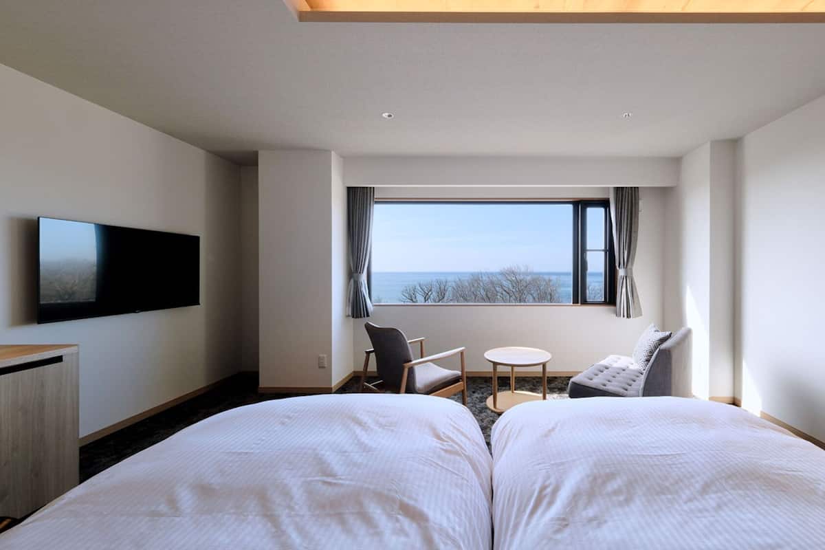 A hotel room with a bed, a TV, a desk, a chair, and a window with a view.