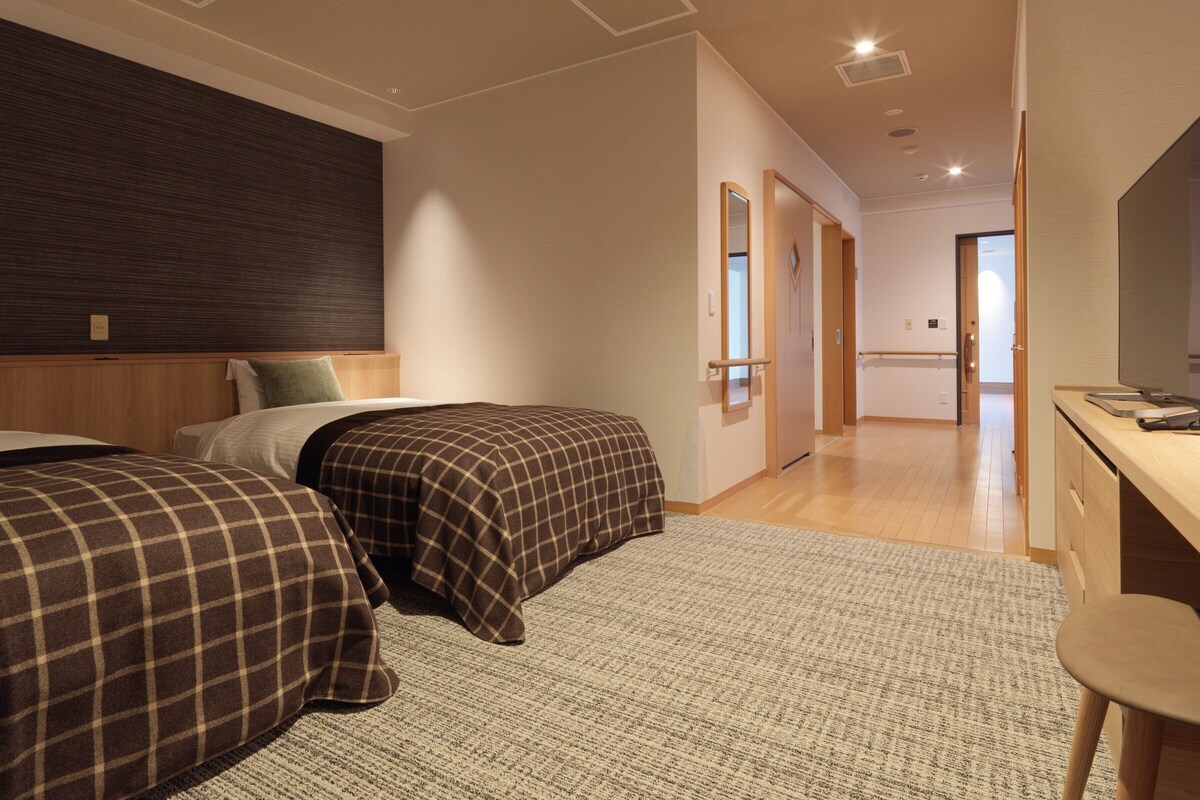 A hotel room with two beds, a desk, and a mirror.