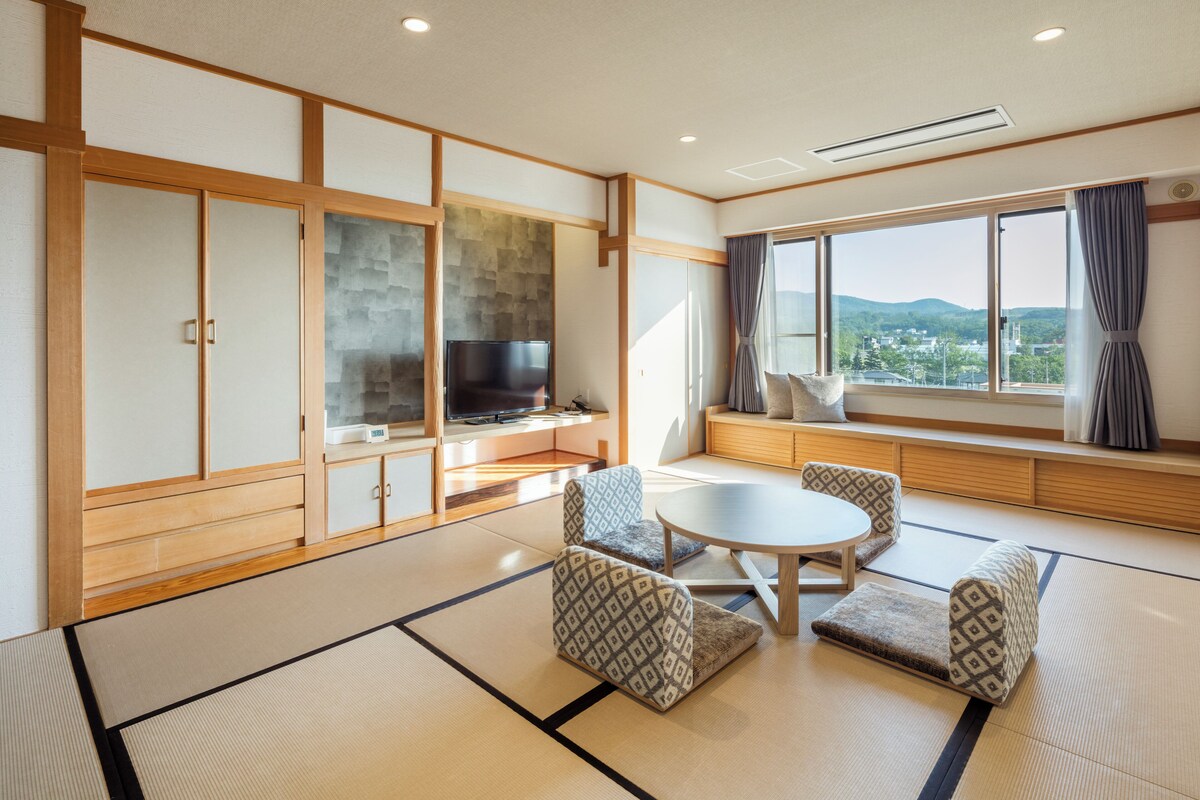 A traditional Japanese-style room with tatami flooring, a low table with cushions, and a television on a wooden cabinet.