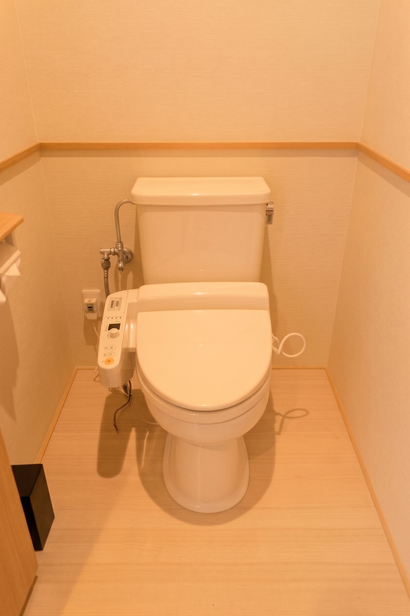 Un inodoro moderno con panel de control, ducha integrada y suelo de madera.