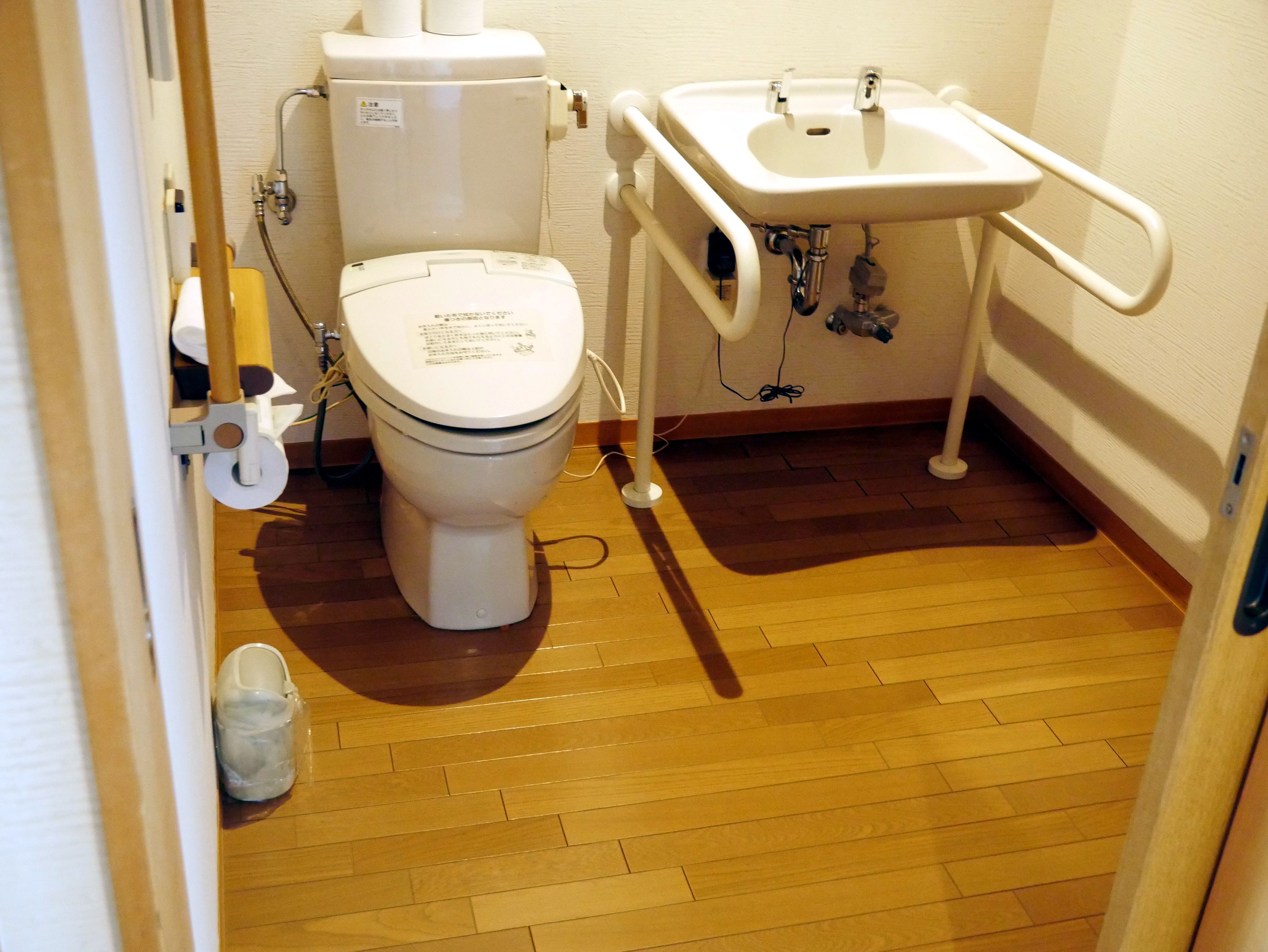 A small bathroom with a toilet, sink, and wooden flooring.