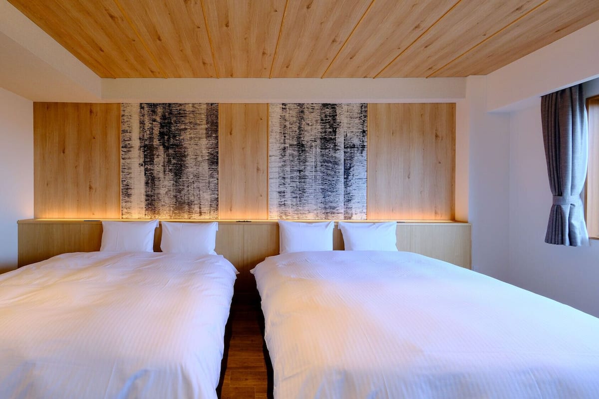 A hotel room with two beds, wooden headboards, and a large abstract painting.