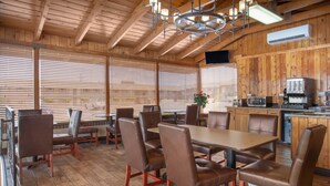 A wooden interior with a dining area featuring a large table and multiple chairs, a kitchen area with appliances, and a television mounted on the wall. - Travelodge by Wyndham Hawthorne (Hawthorne)