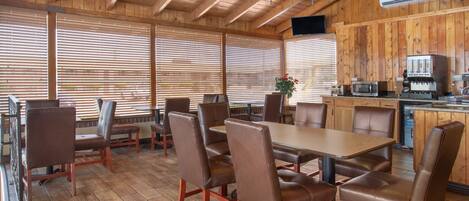 A wooden interior with a dining area featuring a large table and multiple chairs, a kitchen area with appliances, and a television mounted on the wall.