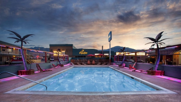 A pool area with lounge chairs and palm trees, a neon sign, and a mountain backdrop. - Travelodge by Wyndham Hawthorne (Hawthorne)