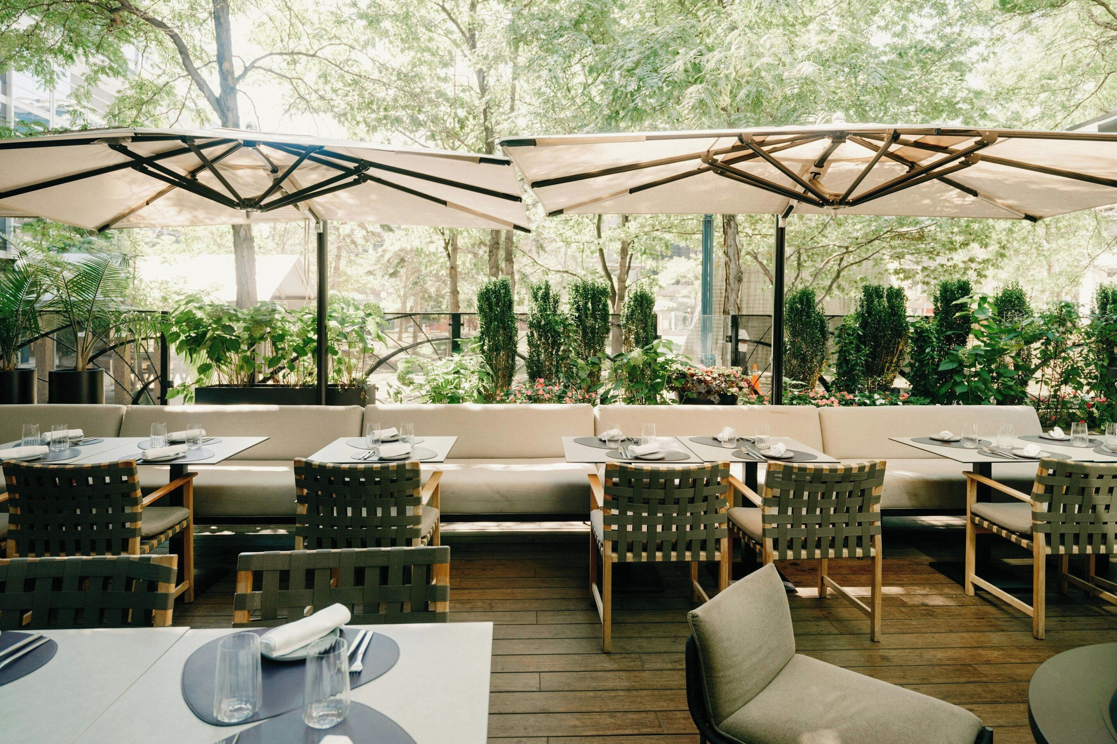 An outdoor seating area with tables, chairs, and umbrellas, surrounded by greenery.
