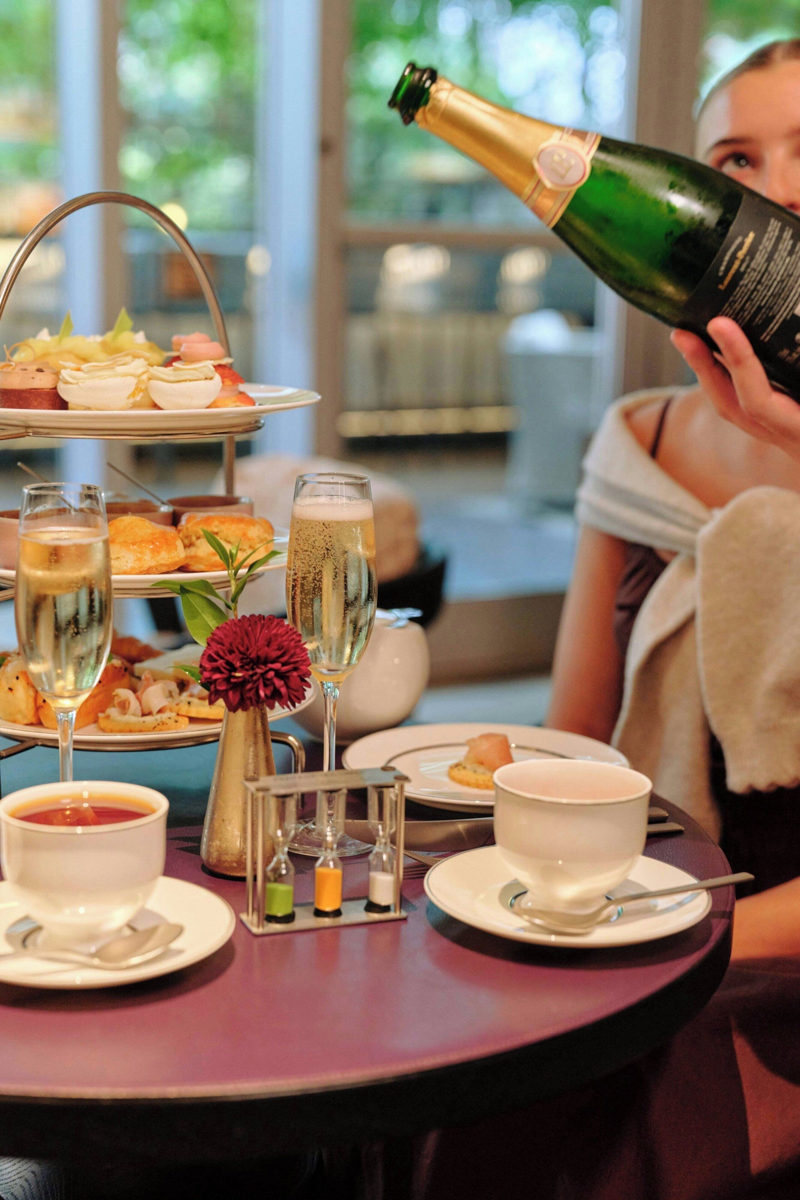 A table set with a bottle of champagne, glasses, a tiered dessert tray, and a vase with flowers.
