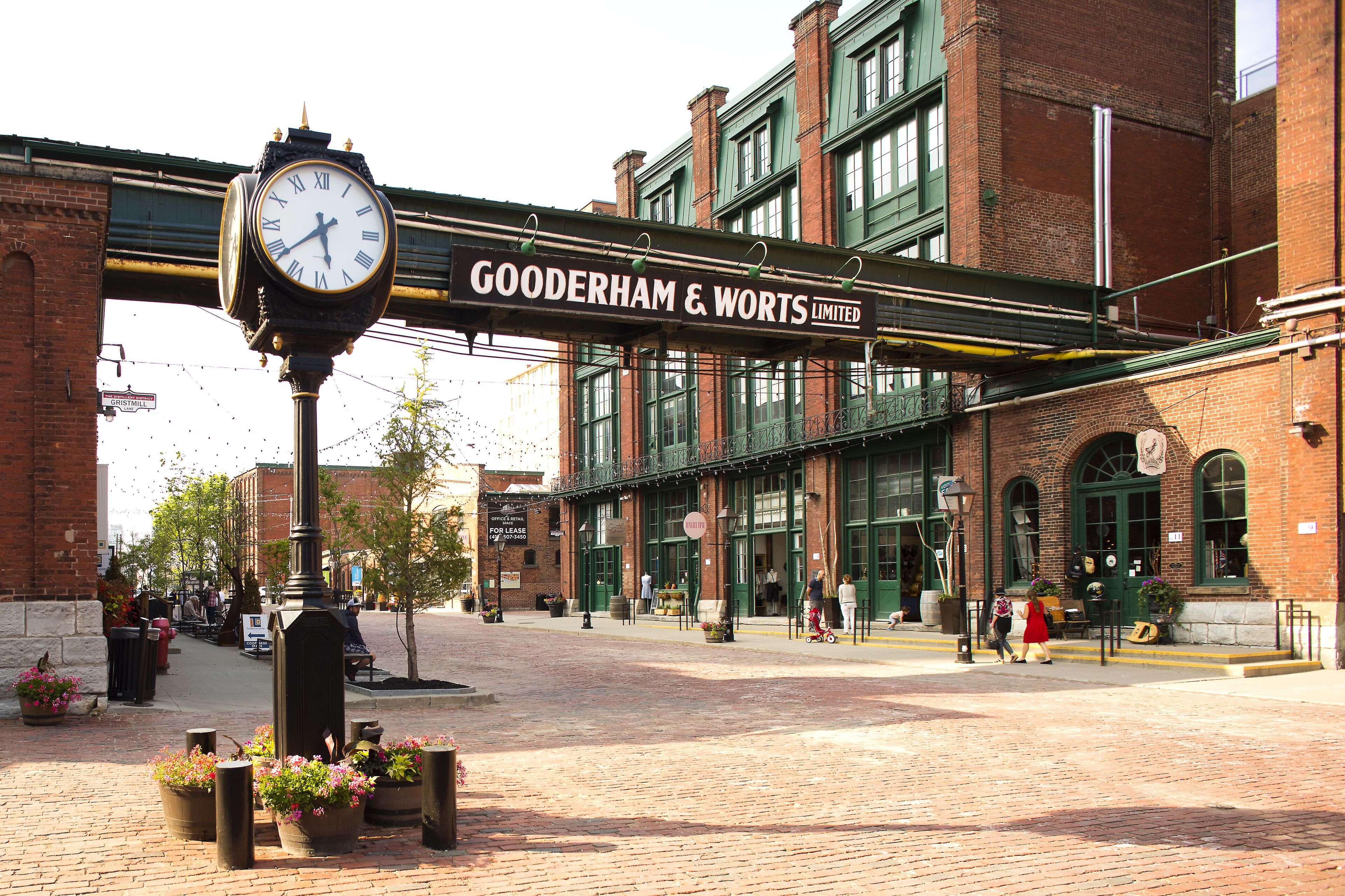 Een klok met een bord erboven met de tekst 'GOODERHAM & WORTS LIMITED' in een openbaar plein met bakstenen gebouwen en potplanten.