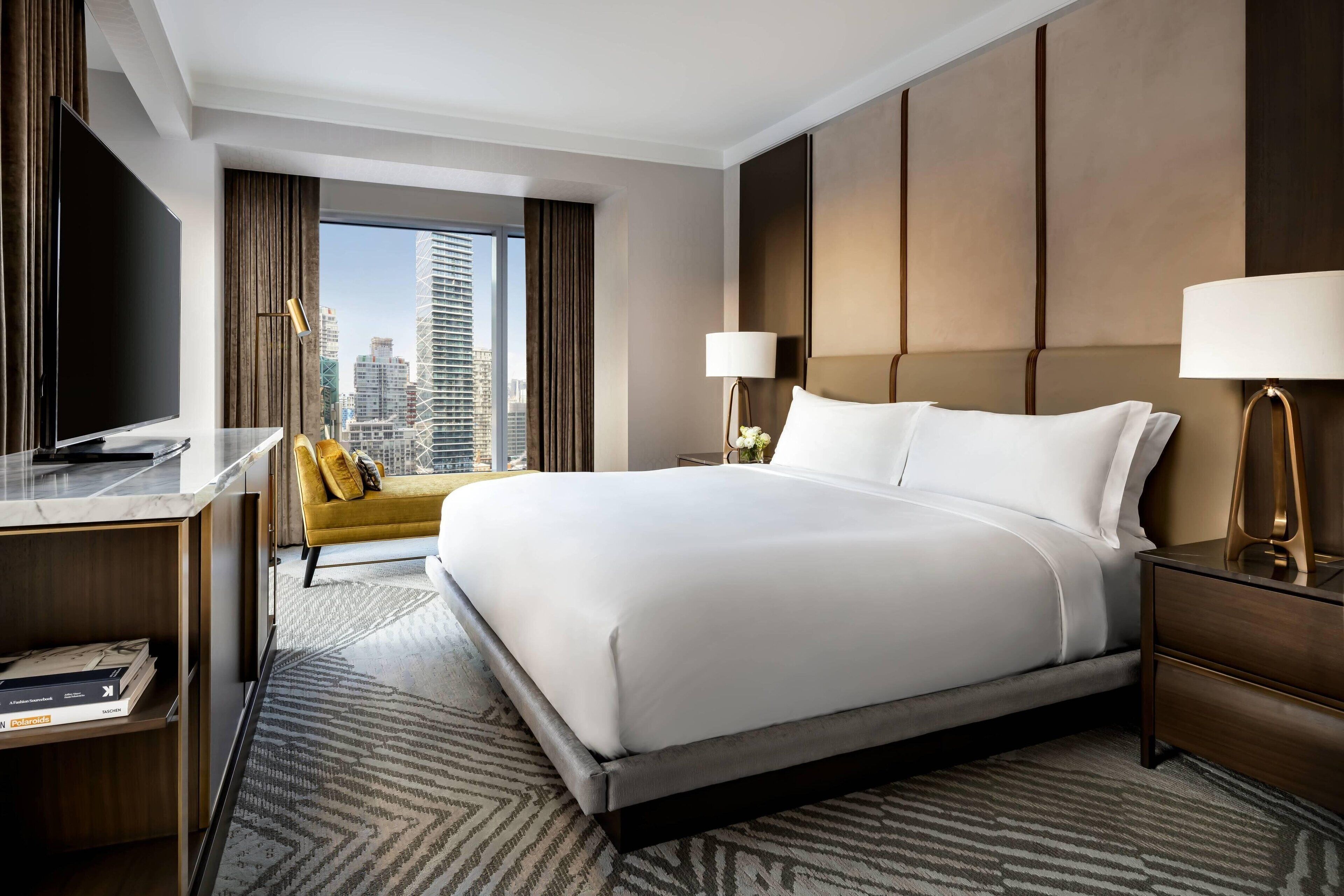 Una habitación de hotel moderna con una cama grande, un escritorio con televisor de pantalla plana, un sofá y vistas al horizonte de la ciudad.