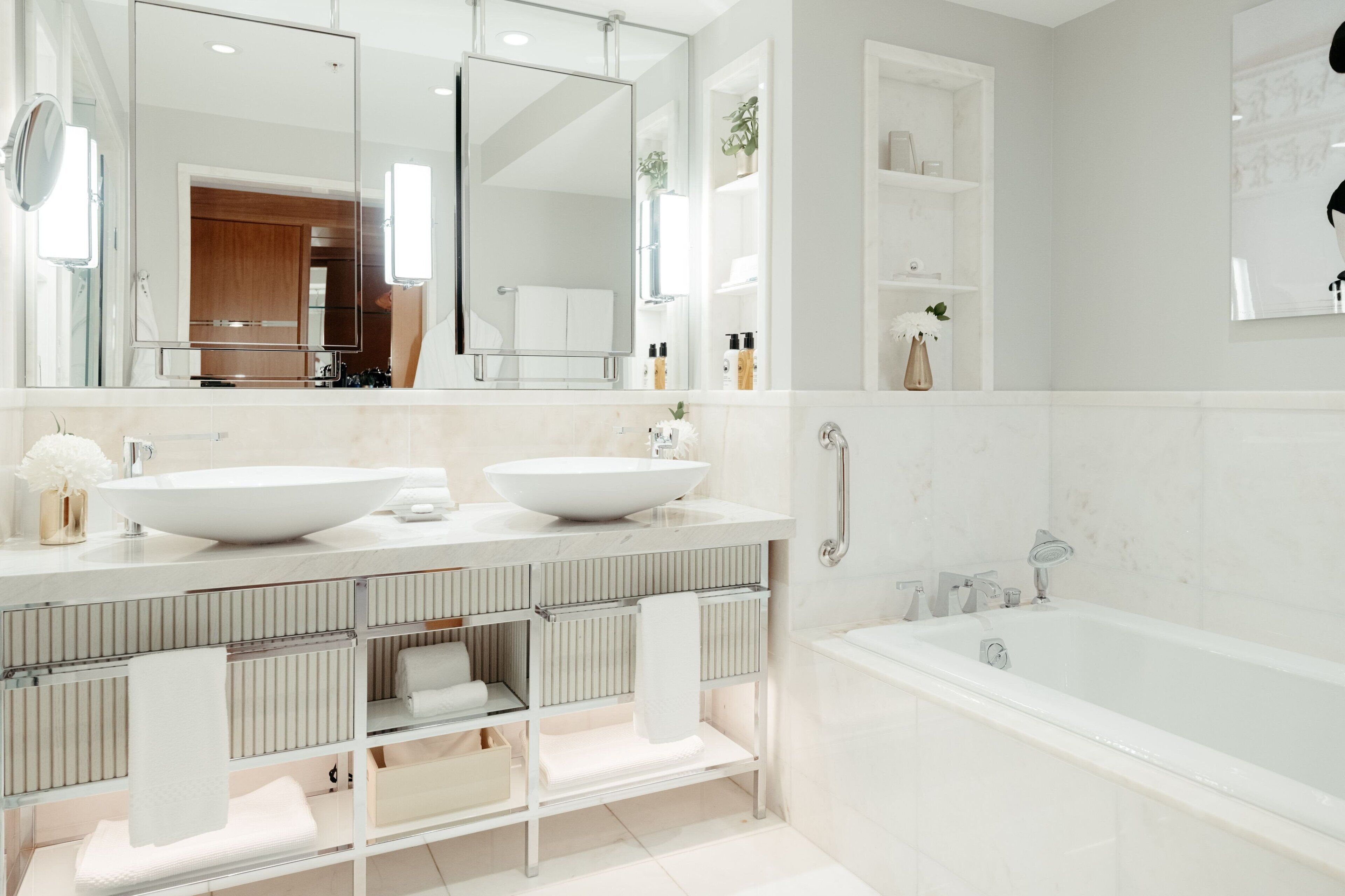 A modern bathroom with two sinks, a large mirror, a bathtub, and a walk-in shower.