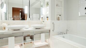 A modern bathroom with two sinks, a large mirror, a bathtub, and a walk-in shower.